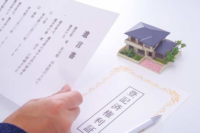 登記済権利証と遺言書を持つ手と家の模型